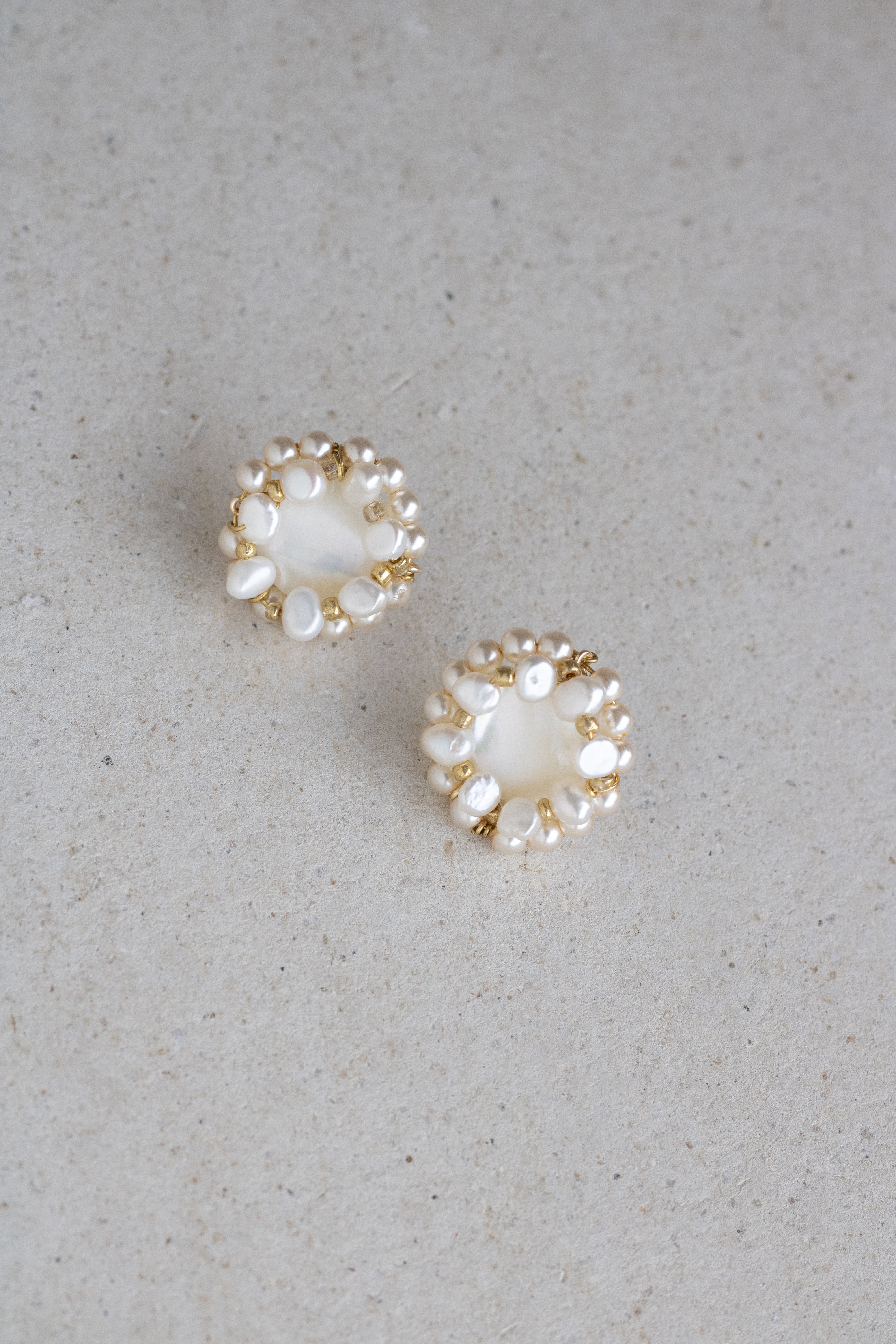 Pair of pearl wedding earrings with pearl and gold accents on a light gray background